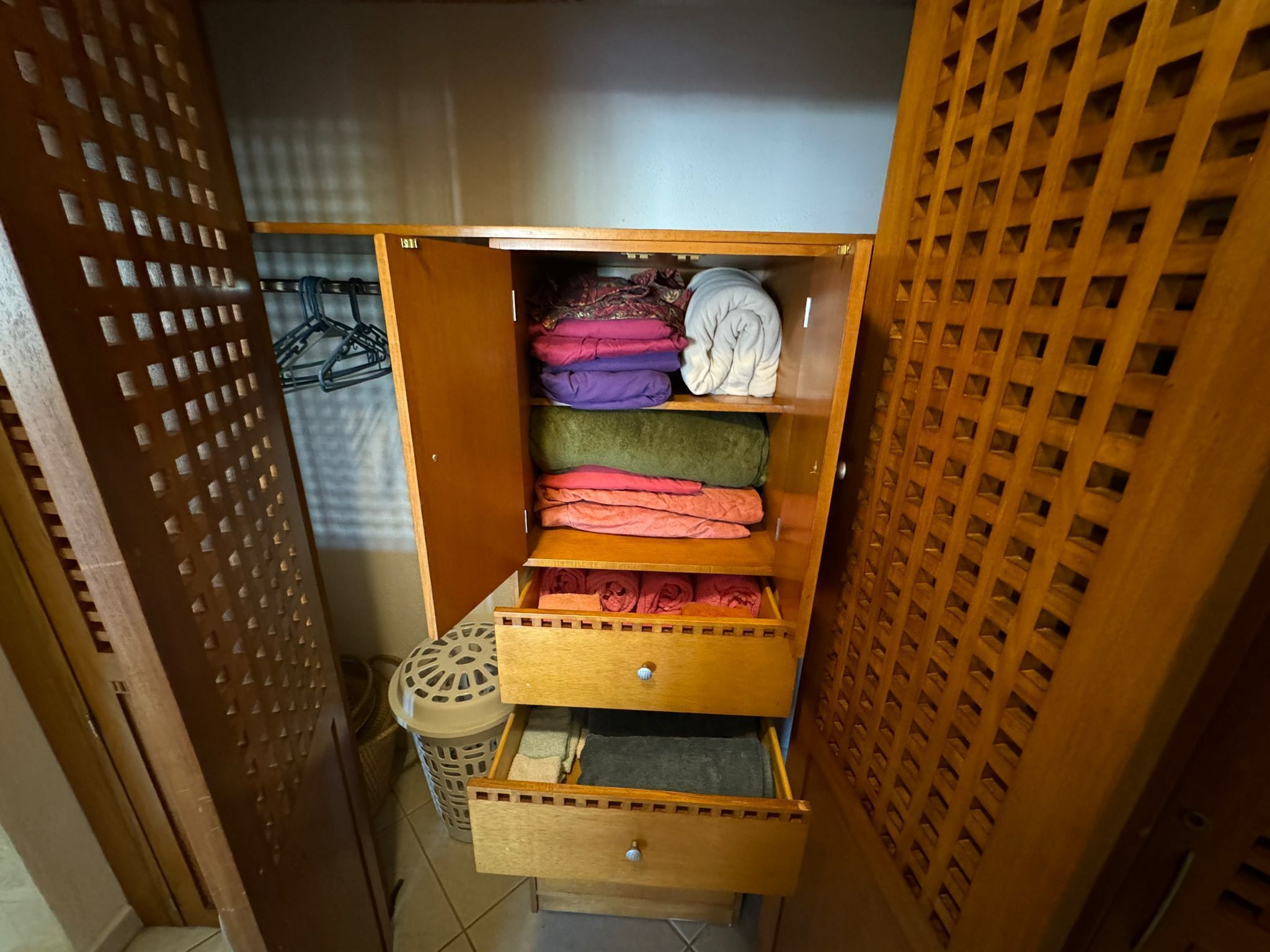 Une armoire en bois dotée de nombreuses étagères et de tiroirs, dans laquelle sont rangés des vêtements pliés.