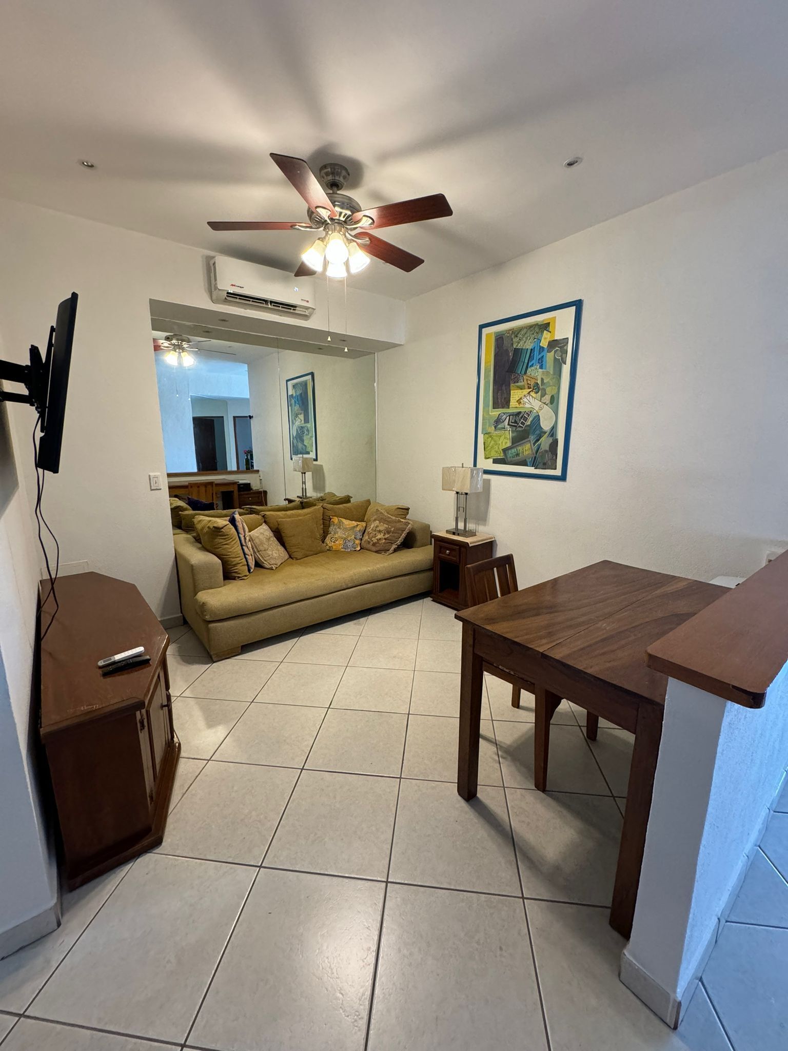 A living room with a sofa, a wooden table, a ceiling fan, and a painting on the wall.