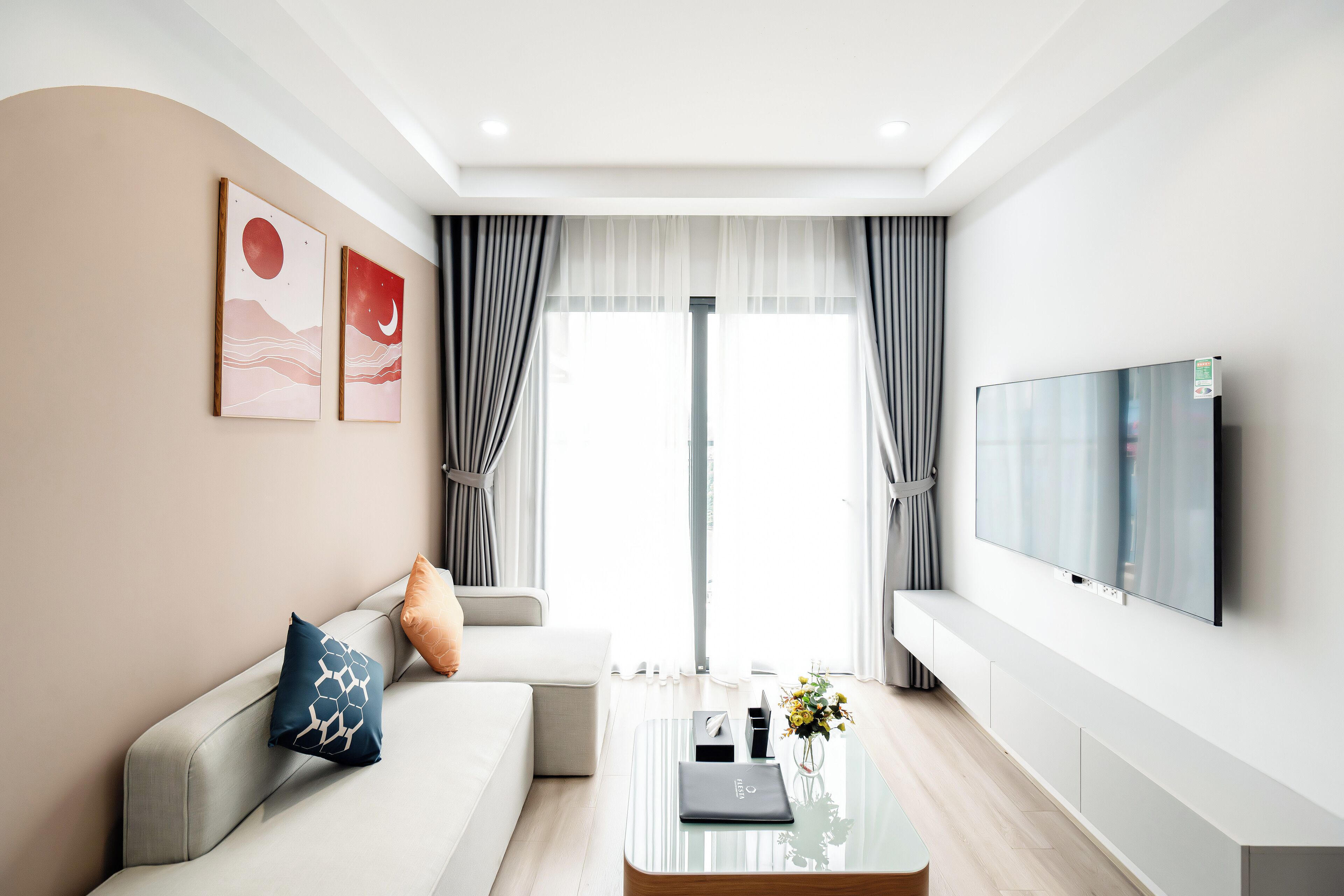 Un salon moderne avec un canapé, une table basse ornée d’un vase et un téléviseur à écran plat fixé au mur.