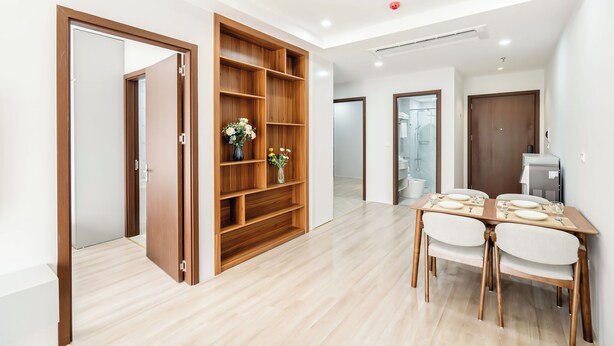 A modern interior with a wooden bookshelf, a dining table with chairs, and a kitchen area. - FLESTA Nui Truc Serviced Apartment & Hotel (Hanoi)
