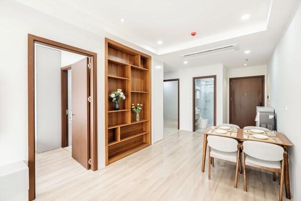 A modern interior with a wooden bookshelf, a dining table with chairs, and a kitchen area.