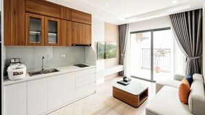 A modern kitchen with white cabinets, a built-in oven, and a sink. There is a dining area with a white table and a sofa with cushions. - FLESTA Nui Truc Serviced Apartment & Hotel (Hanoi)