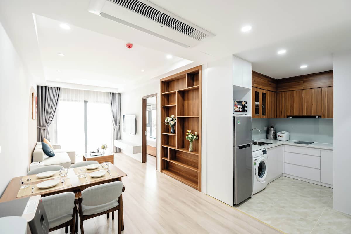 A modern kitchen with a built-in washer and dryer, wooden shelving, and a dining area with a table set for four.