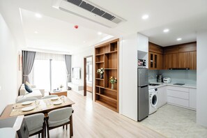 A modern kitchen with a built-in washer and dryer, wooden shelving, and a dining area with a table set for four. - FLESTA Nui Truc Serviced Apartment & Hotel (Hanoi)