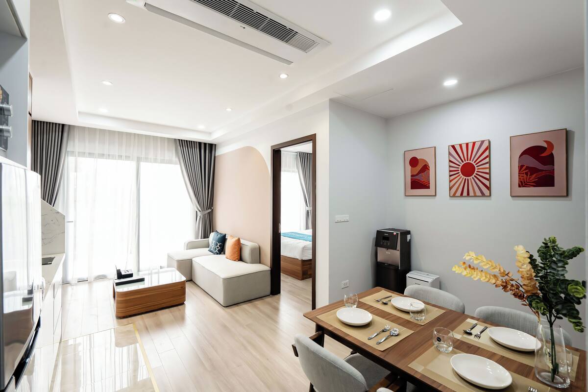 A modern hotel room with a dining area, a living space with a sofa and a bed, and a kitchen area.