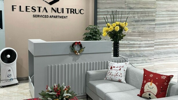 Eine moderne Serviced Apartmentanlage mit Rezeption, einem grauen Sofa, einem rot karierten Hocker und einem großen Fenster mit Blick auf die Stadt.