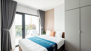A modern hotel room with a large bed, a wardrobe, and a balcony with a view of the city. - FLESTA Nui Truc Serviced Apartment & Hotel (Hanoi)