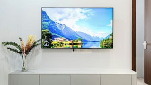 A flat-screen TV mounted on a white wall above a white console with a vase of dried flowers. - FLESTA Nui Truc Serviced Apartment & Hotel (Hanoi)