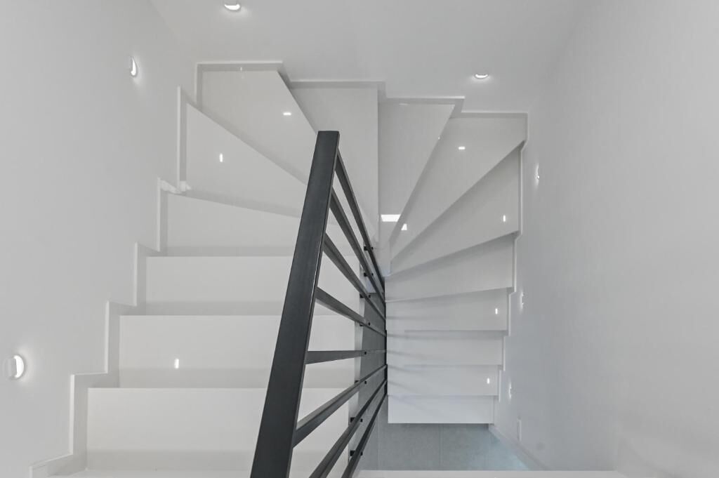 Un escalier moderne au design minimaliste, doté d’une rampe en métal et de murs blancs.