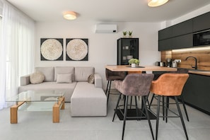 Un salon moderne avec une table basse en verre, un canapé et deux fauteuils. Il y a également un coin cuisine avec une table à manger et des chaises.