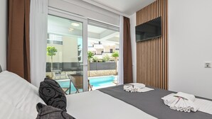 A hotel room with a bed, a TV mounted on the wall, a pool view, and a balcony with a table and chairs. - Smash A - Apartments with private pool  (Novalja)