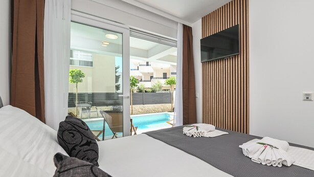 A hotel room with a bed, a TV mounted on the wall, a pool view, and a balcony with a table and chairs. - Smash A - Apartments with private pool  (Novalja)