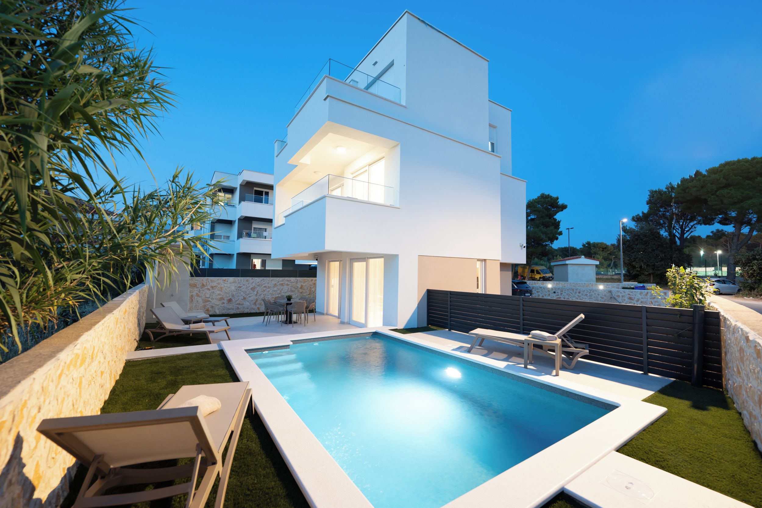 A modern two-story house with a swimming pool, outdoor seating, and a stone wall.