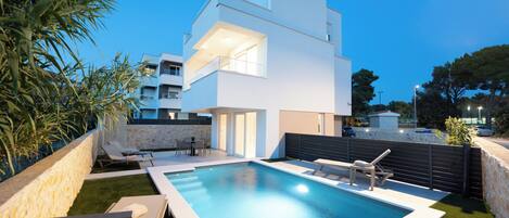 A modern two-story house with a swimming pool, outdoor seating, and a stone wall.