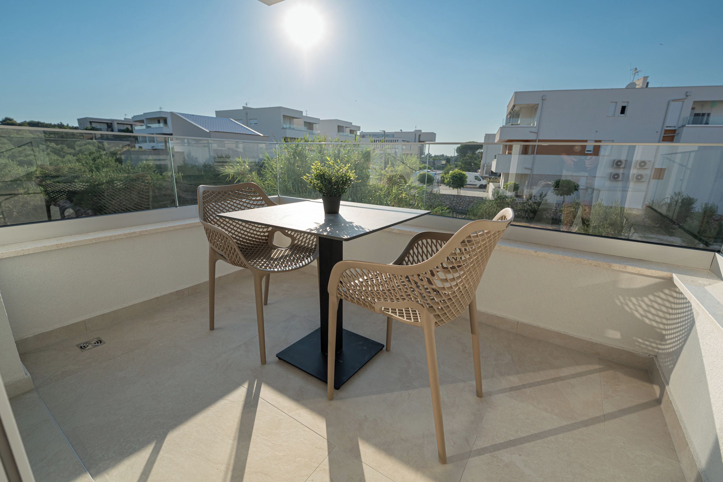A balcony with a table and chairs, a potted plant, and a view of surrounding buildings.