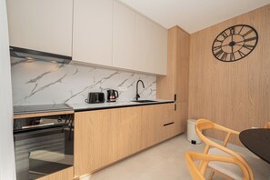 Une cuisine moderne avec des meubles en bois, un pare-feu en marbre, un four encastré, une machine à café et une horloge murale.