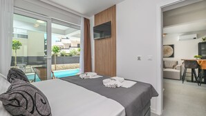 A modern hotel room with a large bed, a TV mounted on the wall, and a view of a swimming pool. - Smash A - Apartments with private pool  (Novalja)