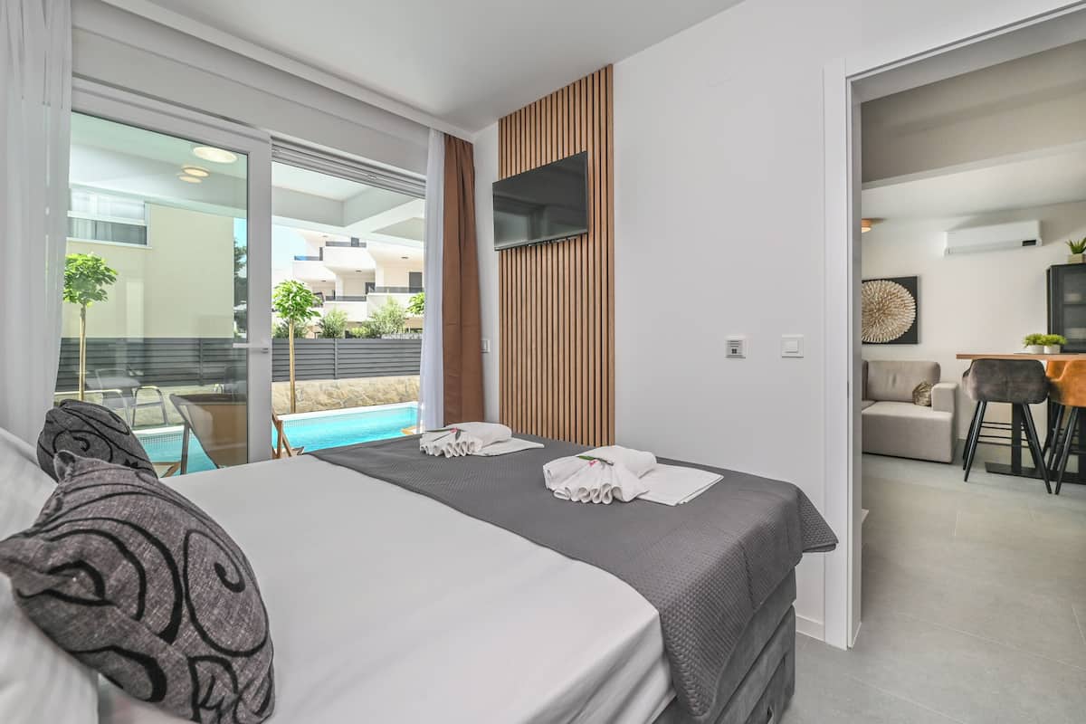 A modern hotel room with a large bed, a TV mounted on the wall, and a view of a swimming pool.