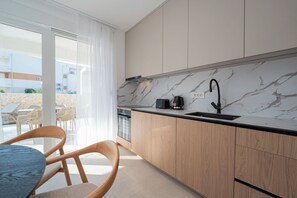 A modern kitchen with a marble countertop, wooden cabinets, a black faucet, and a view of the outdoor seating area. - Smash A - Apartments with Private Heated Pool (Novalja)
