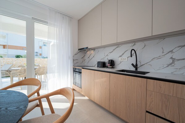 A modern kitchen with a marble countertop, wooden cabinets, a black faucet, and a view of the outdoor seating area. - Smash A - Apartments with Private Heated Pool (Novalja)