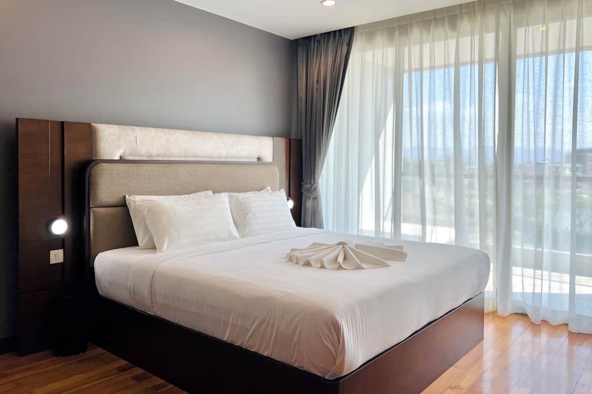 Ein modernes Hotelzimmer mit einem großen Bett, einem Holzkopfteil und Blick auf die Stadt durch transparente Vorhänge.