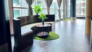 Un vestíbulo moderno con una zona de estar curva, una pequeña mesa redonda con una planta y ventanas amplias con cortinas.