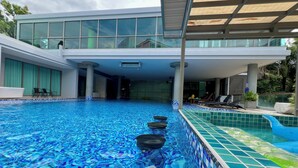 Un hotel moderno con una amplia piscina interior, un área techada con sillones de descanso y vistas a la vegetación circundante.
