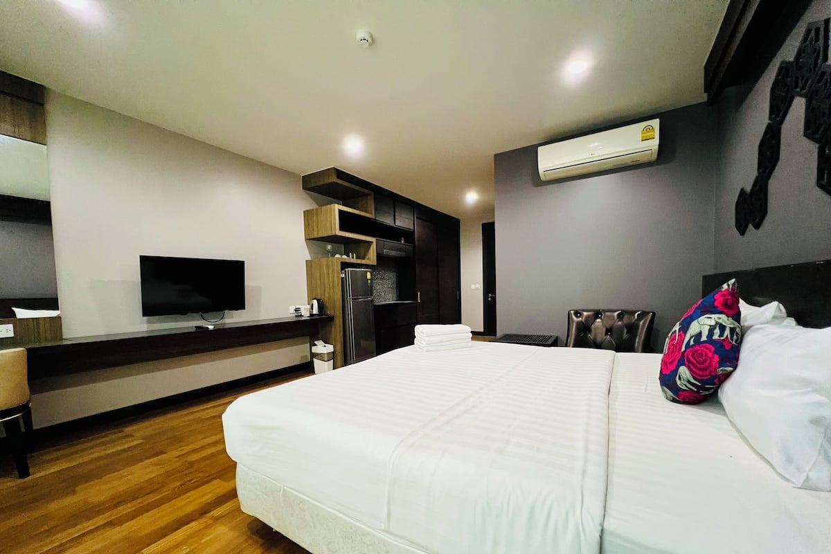 Ein Hotelzimmer mit einem Bett, einem Schreibtisch mit Flachbildfernseher, einer Minikühlschrank, einer eingebauten Klimaanlage und Holzboden.
