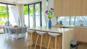 Una cocina moderna con una isla central, taburetes de bar, una zona de comedor con mesa y sillas, y vistas al exterior.