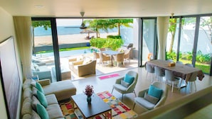 Una sala de estar moderna con un amplio ventanal que da a una vista de la playa, amoblada con sofás, sillas y una mesa de comedor.