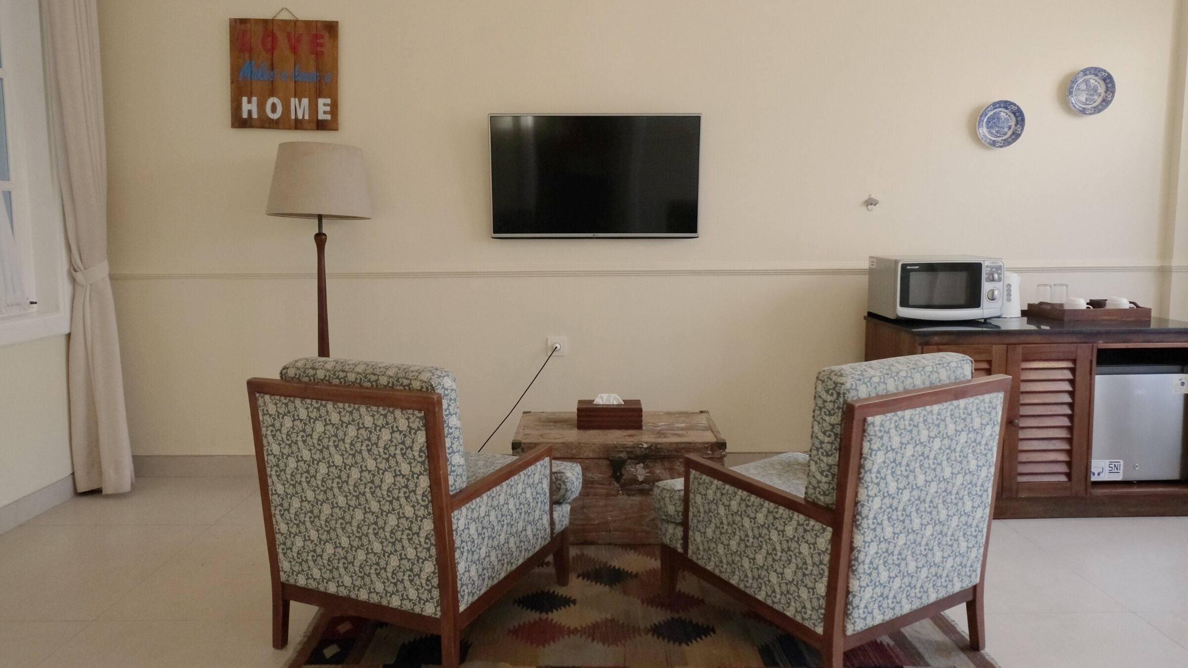 Un salon comprenant deux fauteuils à motifs, une petite table basse, un téléviseur à écran plat, une lampe, un four à micro-ondes et un réfrigérateur.