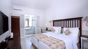 A hotel room with a large bed, a TV, a desk, and a bathroom visible through an open door.
