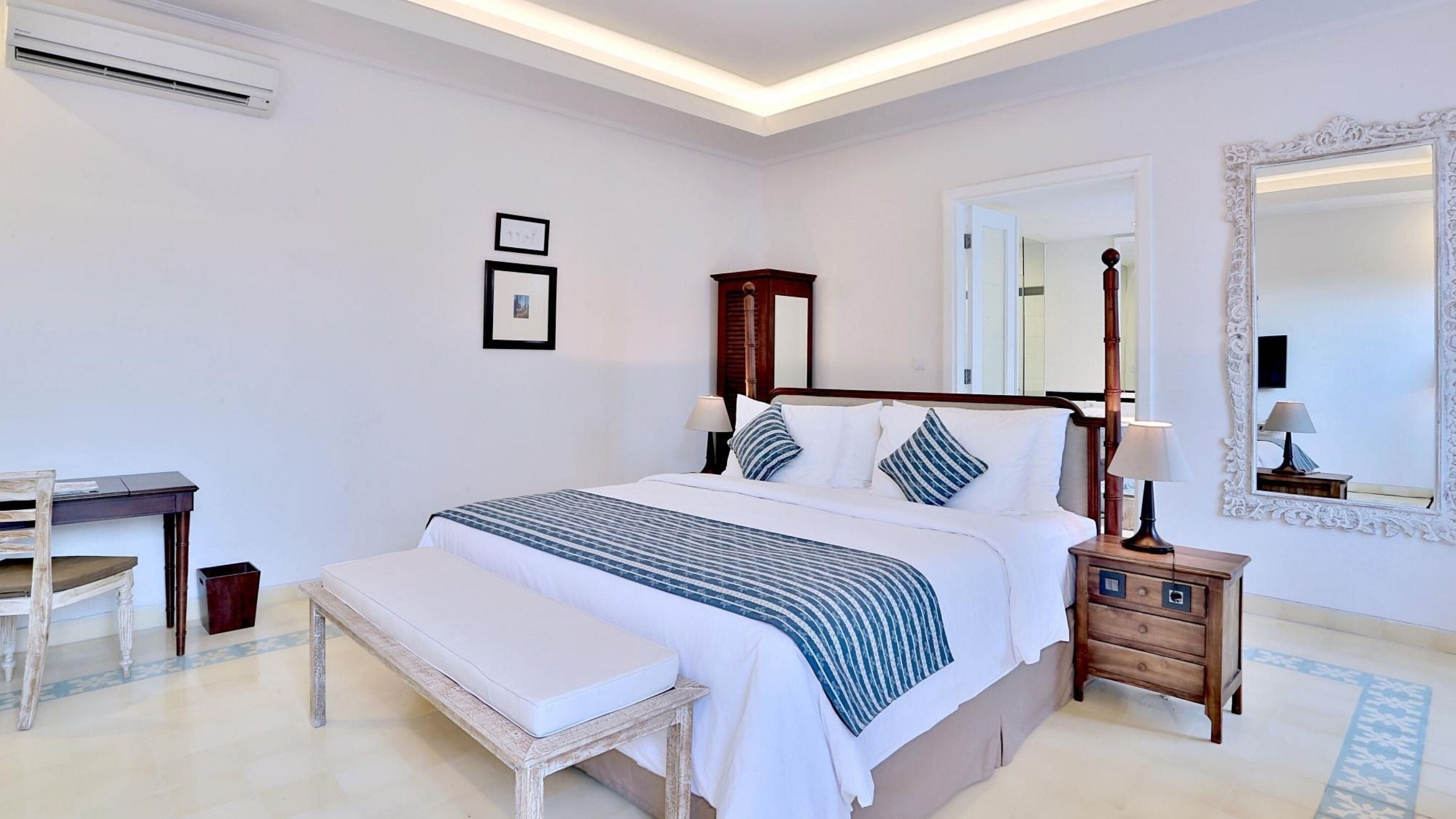 A neatly arranged bedroom with a bed, bedside table, lamp, bench, and a desk.