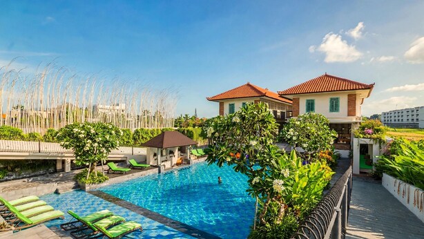 A swimming pool with lounge chairs, a covered seating area, and a building with a red-tiled roof.