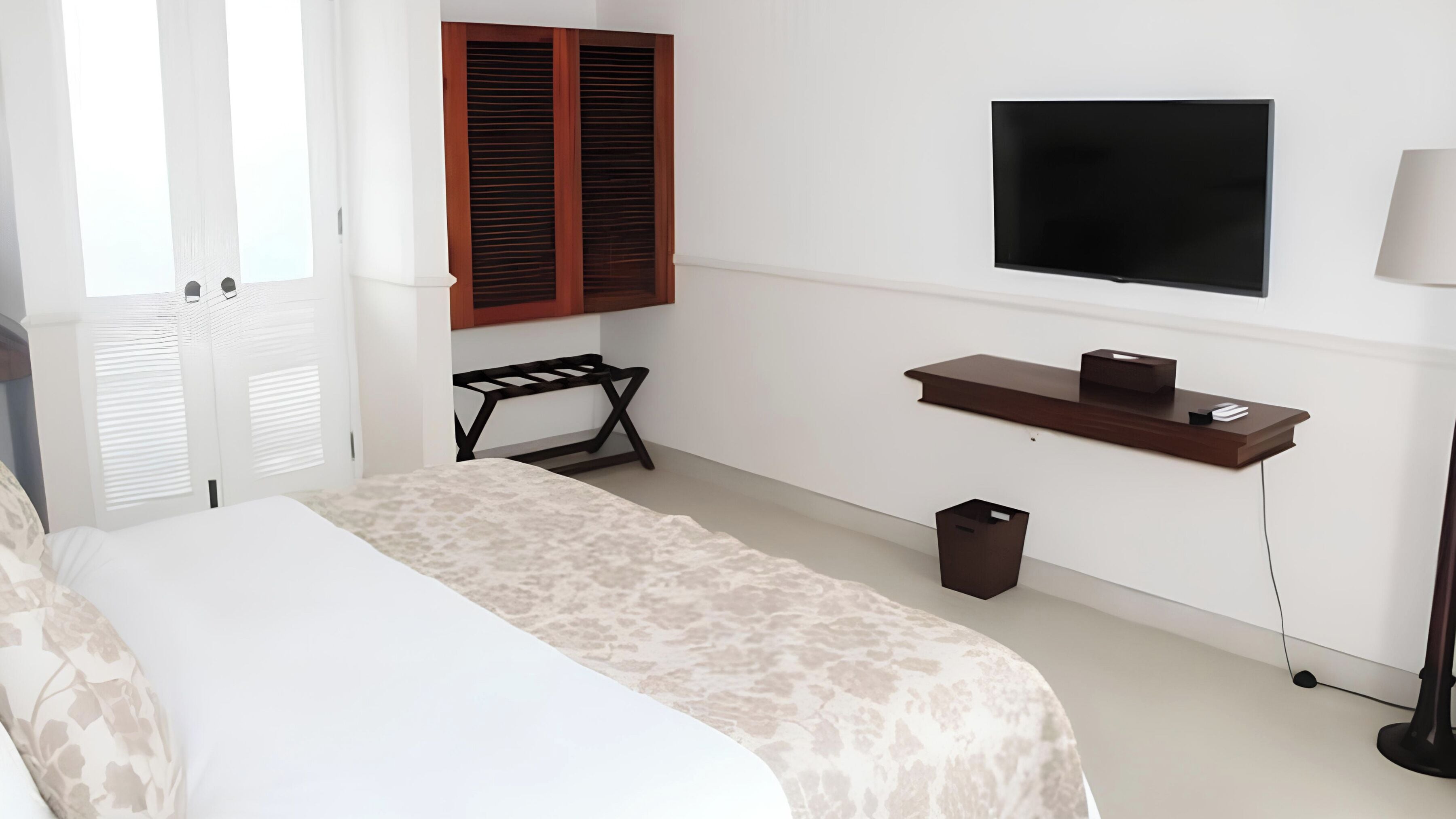 Een slaapkamer met een bed, een bureau, een televisie en een prullenbak.