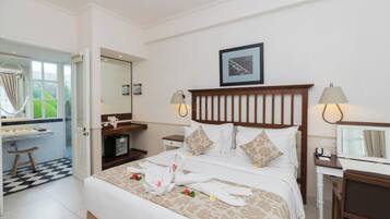 A hotel room with a bed, two bedside tables, a desk with a chair, a mirror, and a window with curtains.