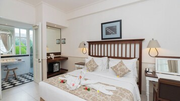 A hotel room with a bed, two bedside tables, a desk with a chair, a mirror, and a window with curtains.