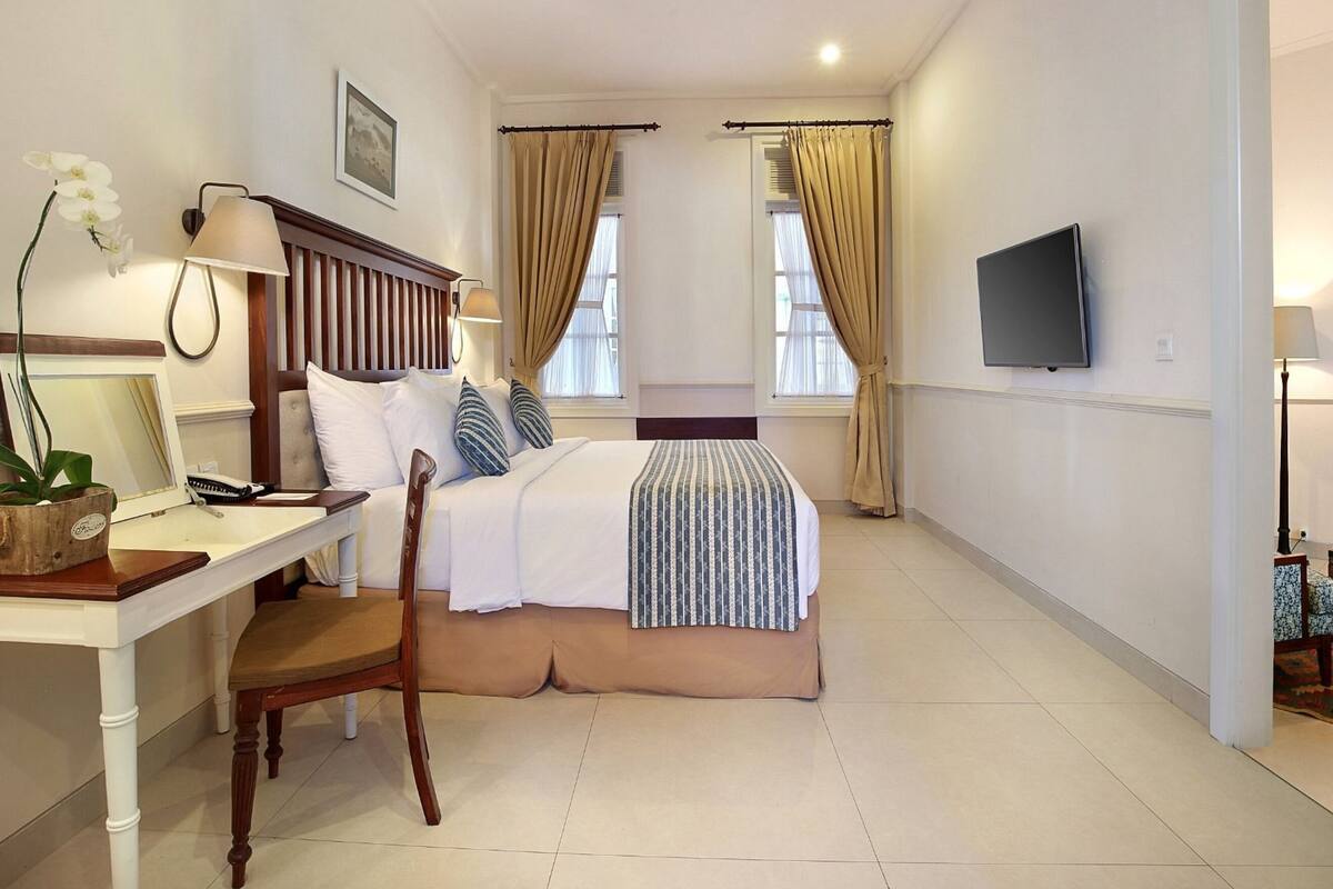 A hotel room with a bed, bedside table, desk, chair, TV, and a small table with a plant.