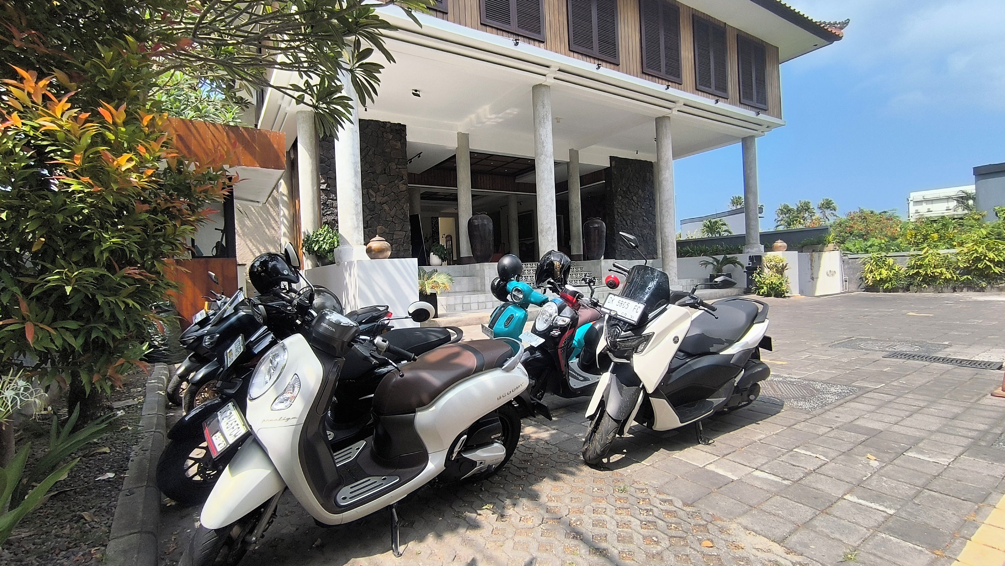 Un espace de stationnement avec deux scooters, un bâtiment doté de colonnes et un mur en pierre.