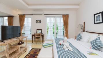 A hotel room with a bed, a desk with a TV, a chair, and a window with curtains.