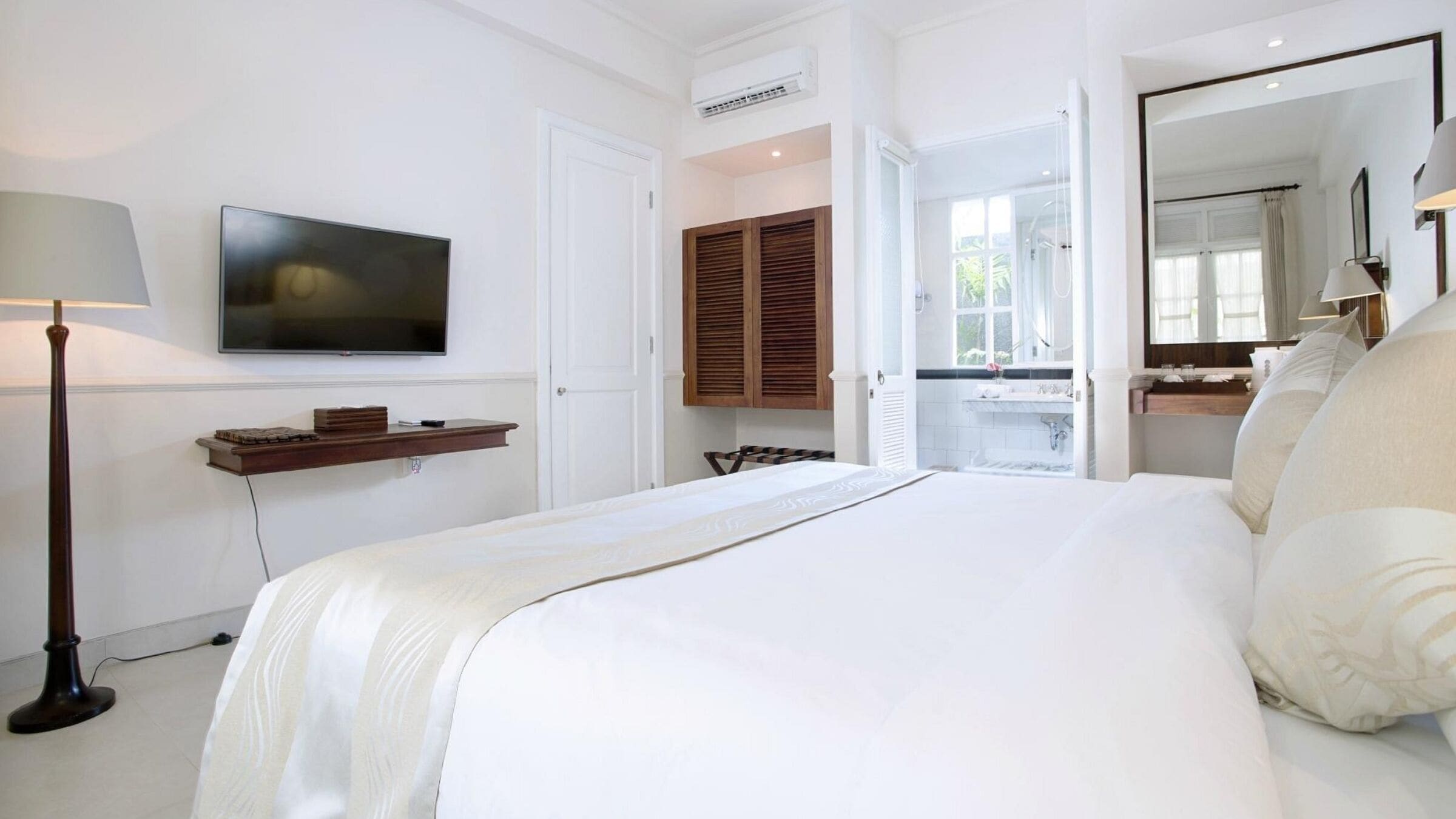 A hotel room with a large bed, a TV mounted on the wall, a wooden cabinet, and a bathroom visible through an open door.