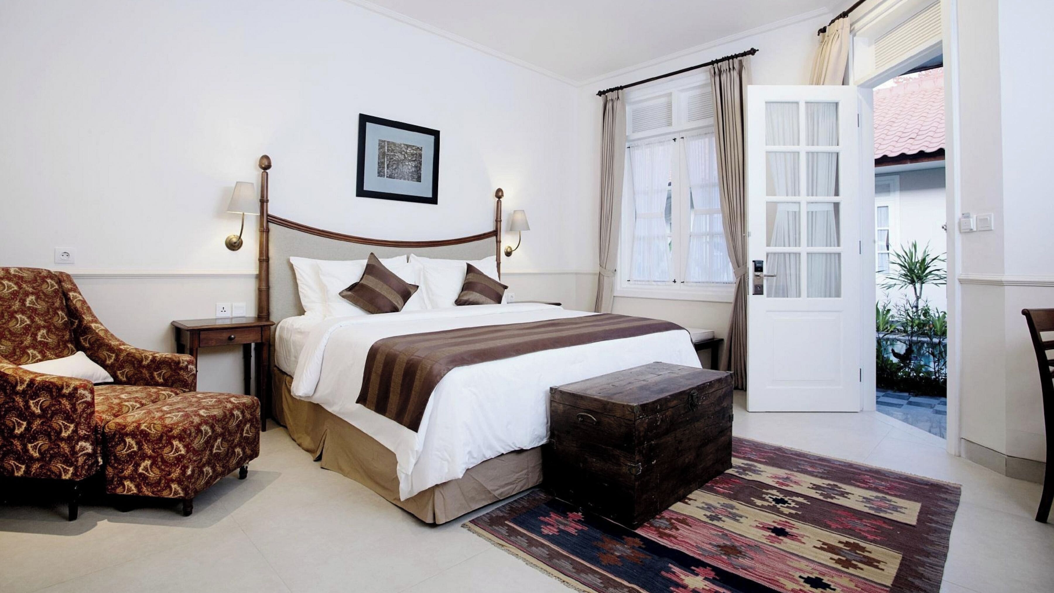 A bedroom with a bed, a chair, a bedside table, a rug, and a door leading to a balcony.