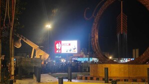 A nighttime outdoor area with a large illuminated billboard, a decorative metal structure, and a paved walkway. - Vedas Villa (Faizabad)