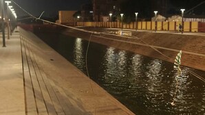 A nighttime view of a riverside walkway with a wooden deck and a bridge over water. - Vedas Villa (Faizabad)