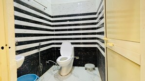 A small bathroom with a toilet, a sink, and a blue bucket. - Vedas Villa (Faizabad)