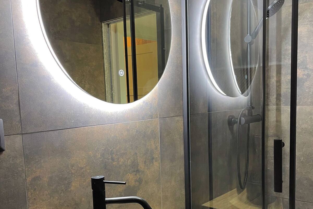 Une salle de bain moderne avec un grand miroir rond, un lavabo noir et une douche à parois de verre.