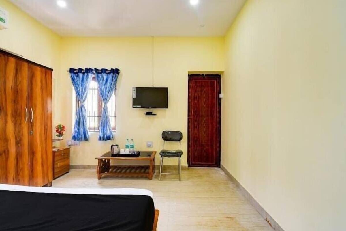 Una habitación con una cama, un armario de madera, un televisor, una puerta roja y una ventana con cortinas azules.