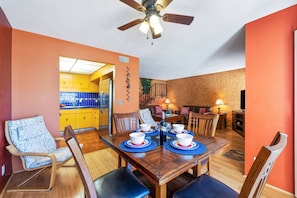A dining area with a wooden table set for four, surrounded by chairs. A ceiling fan is visible above the table.