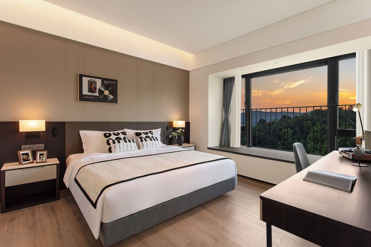 Ein modernes Hotelzimmer mit einem großen Bett, einem Schreibtisch, Blick auf den Sonnenuntergang und einem gerahmten Bild an der Wand.