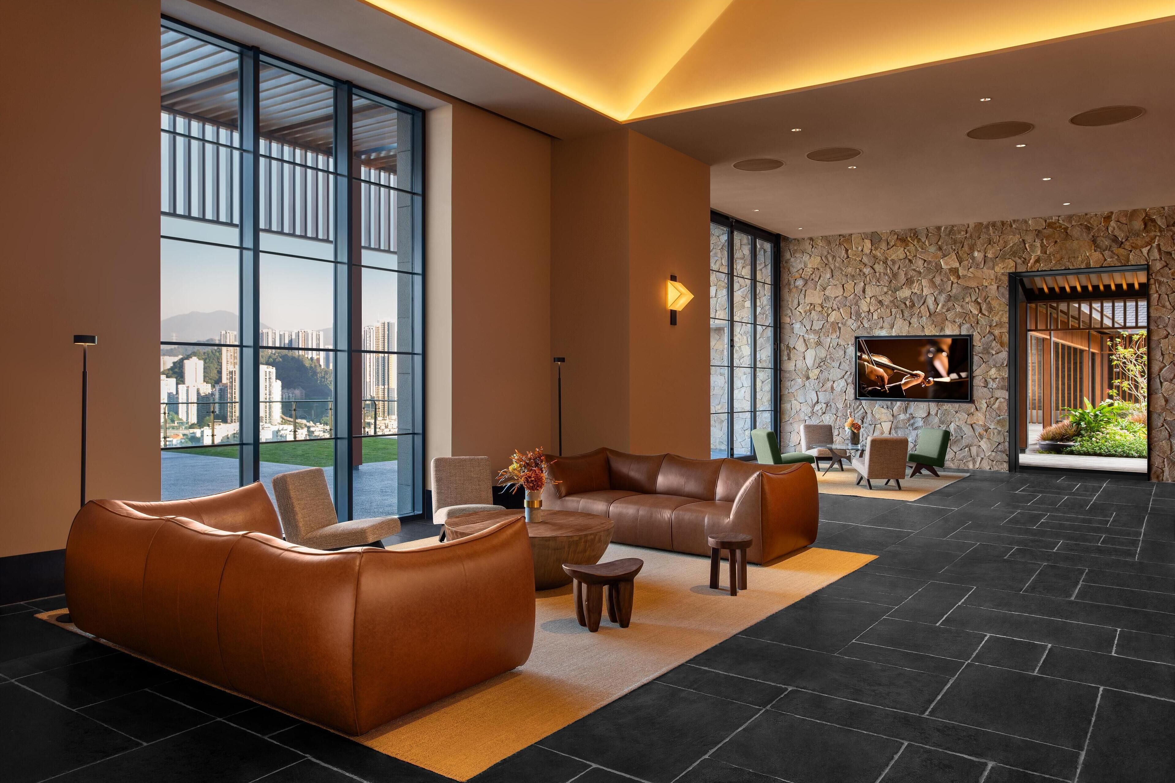 A spacious lobby with large windows, a leather sofa, a coffee table, and a TV screen.